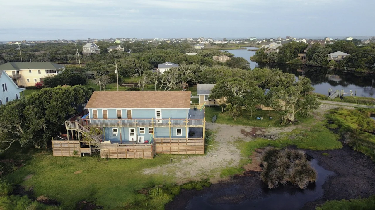 A blue coastal home with white balconies beside marsh and a pond on Hatteras Island